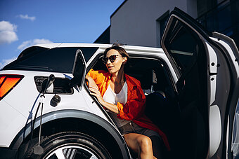 THG-Quote Firmenwagen. Frau sitzt im ladenden E-Auto 