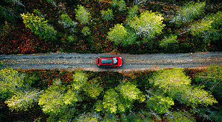 E-Auto unterwegs laden. Rotes E-Auto fährt auf Waldweg