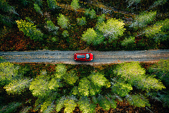 E-Auto unterwegs laden. Rotes E-Auto fährt auf Waldweg