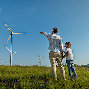 Grüner Wasserstoff von Westfalen. Vater und Sohn stehen in Wiese vor Windkraftanlage