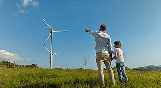 Grüner Wasserstoff von Westfalen. Vater und Sohn stehen in Wiese vor Windkraftanlage