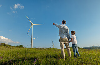 Grüner Wasserstoff von Westfalen. Vater und Sohne auf Feld vor Windkraftanlage