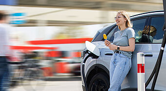 E-Auto unterwegs laden. Junge Frau steht vor Ihrem ladenden E-Auto