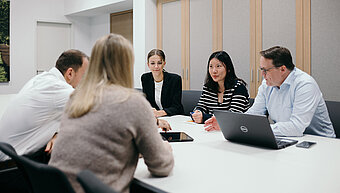 Schulungen zum Thema Compliance. Mitarbeiter sitzen gemeinsam in einem Meeting an einem großen Tisch 