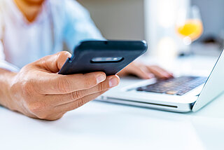 Westfalen Tankstellen Kundenportal. Mann sitzt mit Handy am Laptop